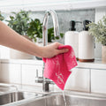 Pink Cellulose Dish Cloth dripping of soapy water and being wrung out and held over filled sink with bubbled in a kitchen environment