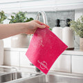 Pink Swedish Dish Cloth dripping of soapy water, being held over filled sink with bubbled in a kitchen environment