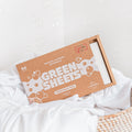 The Green Company unscented laundry detergent 64 load pack sitting in a wicker laundry basket with some clean, white bed linen