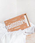 The Green Company unscented laundry detergent 64 load pack sitting in a wicker laundry basket with some clean, white bed linen