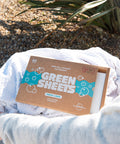 the green company vegan laundry detergent sheets, fresh linen 64 load pack outside in a washing basket, resting on 3 white towels